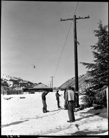 Linemen working working on pole line in the snow with helicopter flying near by