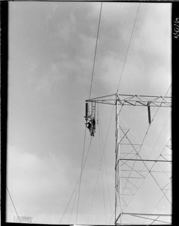 Men hanging from tower crossarm stringing conductor