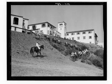 Boys riding horses toward campus buildings, Urban Military Academy, Brentwood, Los Angeles
