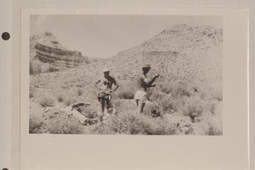 Dock Marston and Norm Nevills examining the cache left by thDock Marston picks up items from plane-drop halfway to the top of the Archean at Mile 99 1/2e aviation crew on the platform below Point Sublime