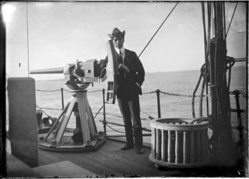 Man posed on a naval vessel, leaning on a gun