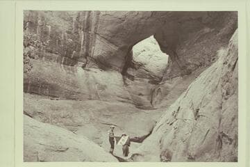 Masland and Marston holding Explorers Club flag at natural bridge in Navajo Canyon.  Masland proposes name, "Ba-Sah Bridge," for the seven pot-holes below it
