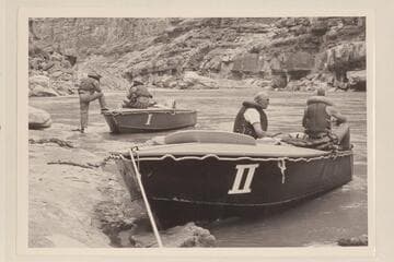 The two 18-ft. boats of the outboard fleet of the 1953 traverse of the Canyons.  Bill Belknap sits on the I.  Ed Ralph talks with Don Harris in the II.  Note the boulder of Boulder Narrows in the background.  Flow approximates 50,000 cfs