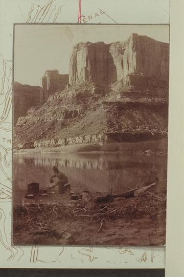 Camp below mouth of Hell Roaring Canyon.  Taken during trip in 1901-1902 from Greenriver, Utah, to Rapid #3 in Cataract Canyon.  Probably Arthur O. McCormick in the scene.  The Wingate in the background is part of the Twin Fortress