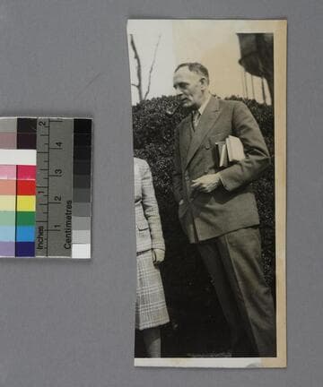 Edwin Powell Hubble wearing a double-breasted suit, with books in his left arm and a pipe in his mouth