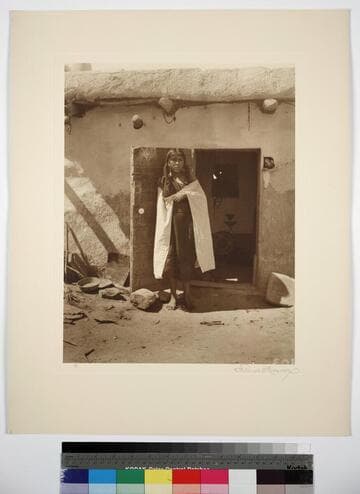A young Hopi woman standing in doorway of adobe building
