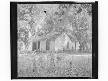 Unidentified house with family group near door, well and pump in yard