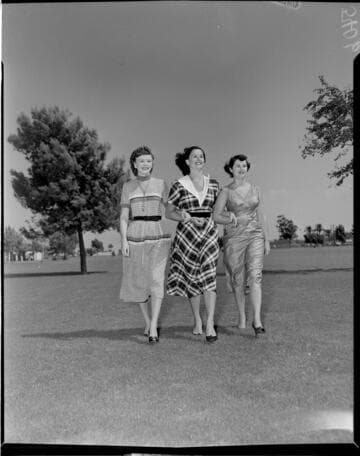 Three young ladies in skirts and sweaters walking arm & arm towards camera at the park