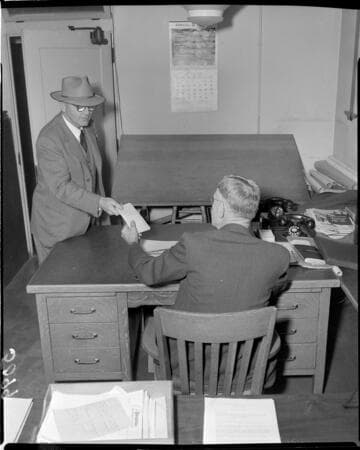 Man handing folded paper to man at desk