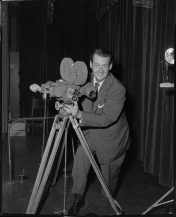 Cinematographer with large reel 16mm movie camera on tripod set