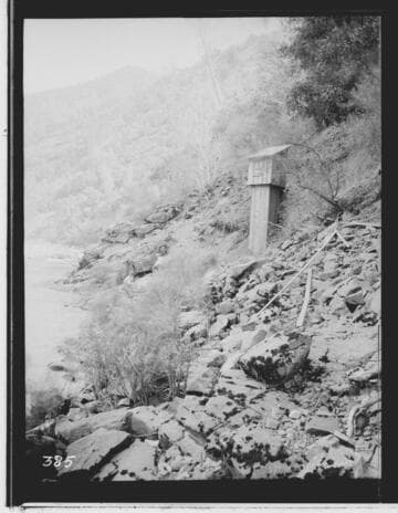 Cabin on a hillside with person sitting on rocks nearby