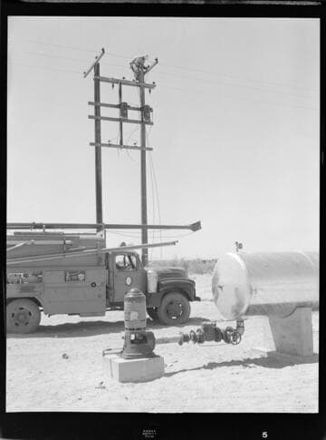 Linemen installing transformers on a pair of distribution poles in the desert