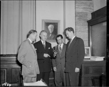 Four men in an office with a painting of Edison on the wall