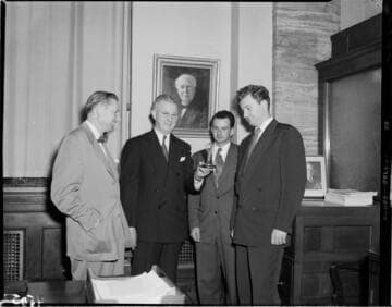 Four men in an office with a painting of Edison on the wall