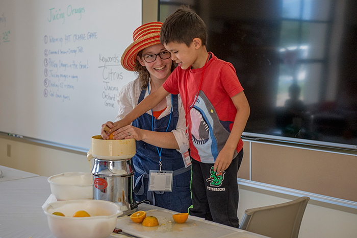 Emily Earhart helps a student juice a just-picked orange. Photo by Martha Benedict.